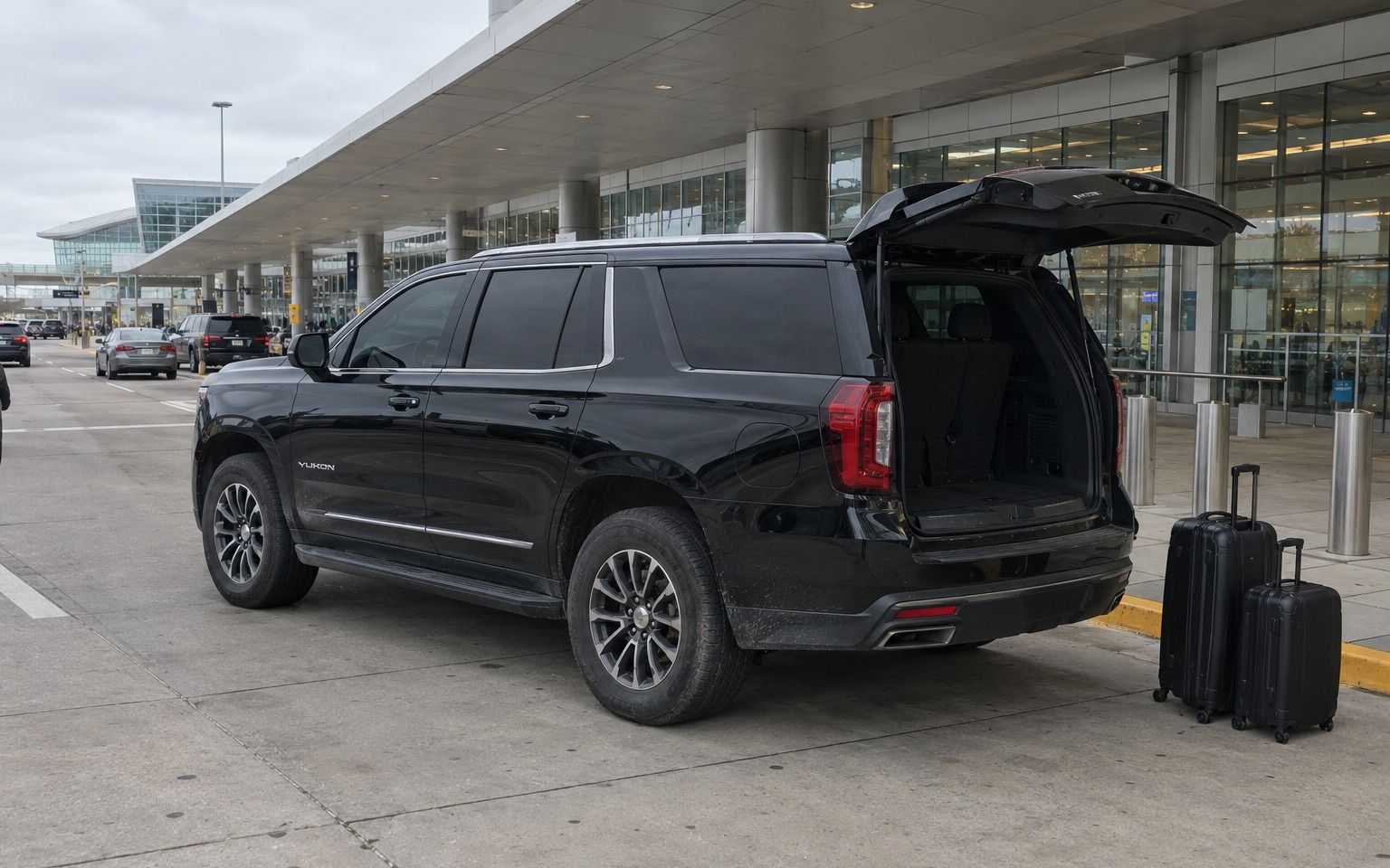 Black SUV with its tailgate open and two suitcases at an airport curb