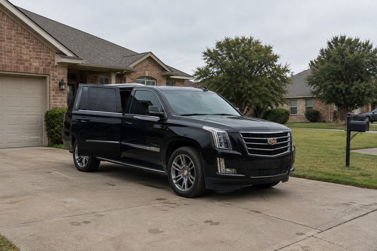 Black Cadillac Escalade parked in the driveway of a brick suburban home