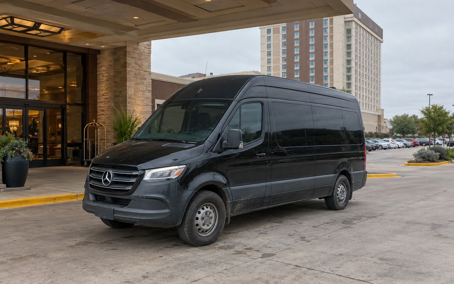 Black Mercedes-Benz Sprinter van parked under the entrance canopy of a resort hotel