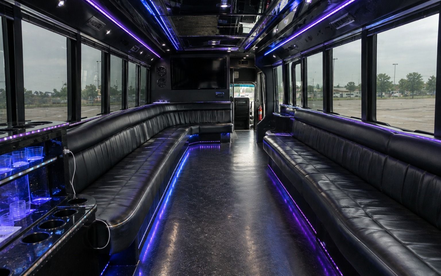 Black leather seats along both sides of a party bus lit with purple LEDs