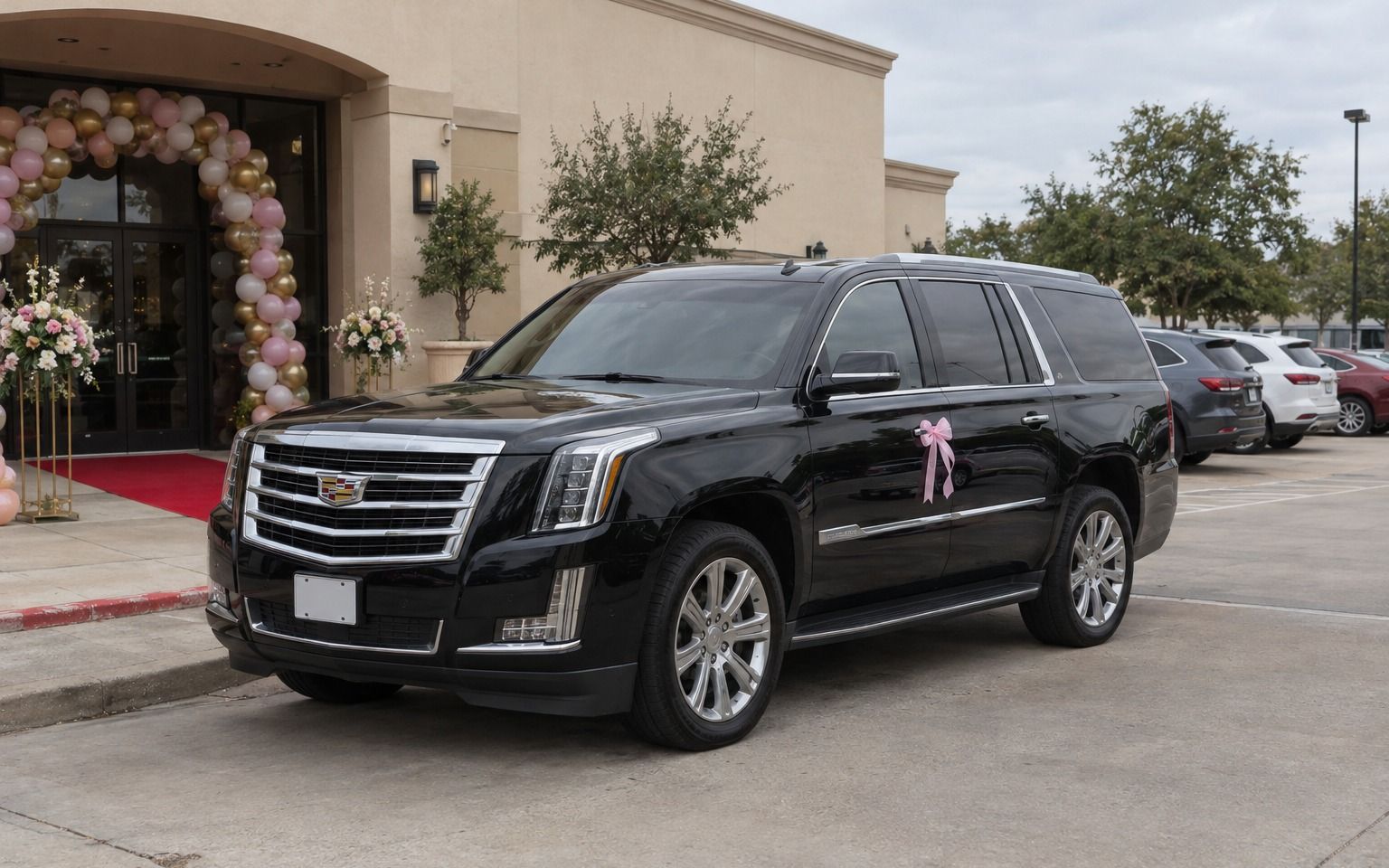 Black Cadillac Escalade with a pink bow outside a venue decorated with balloons